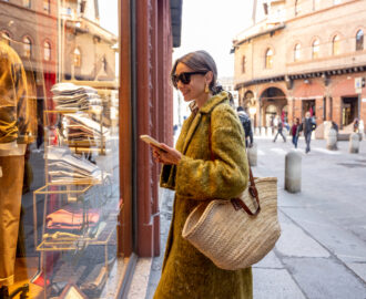 Stylish woman stands near the showcase of the shop with luxury clothes on street in Bologna city. Italian style and shopping concept